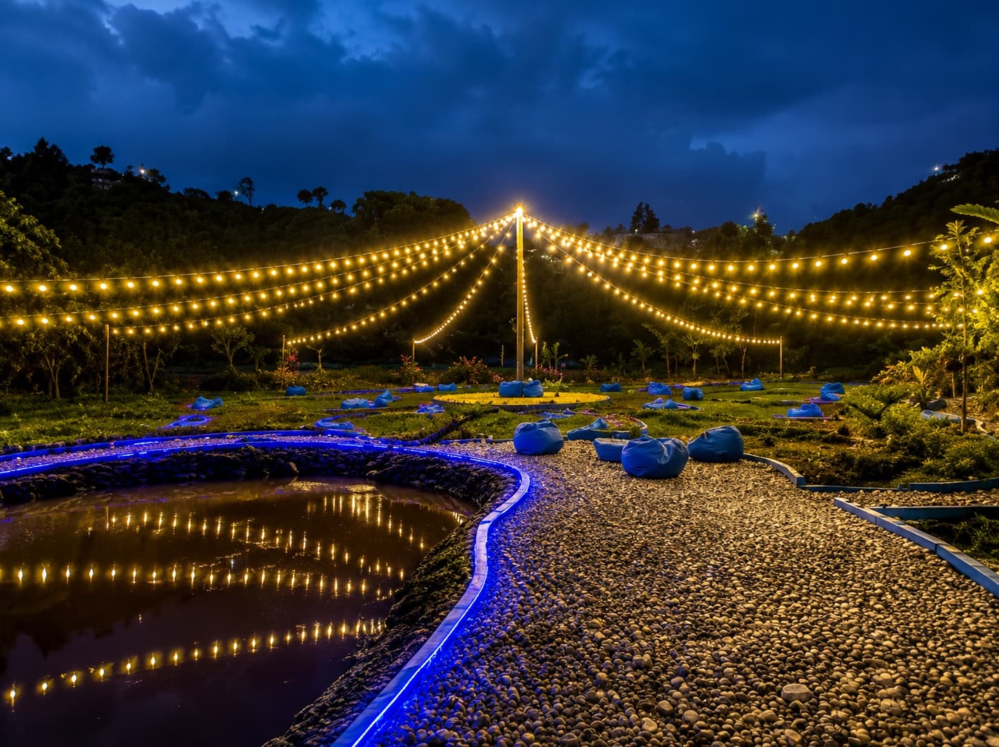 Zona de encuentro iluminada con luces colgantes y reflejos en el lago al anochecer