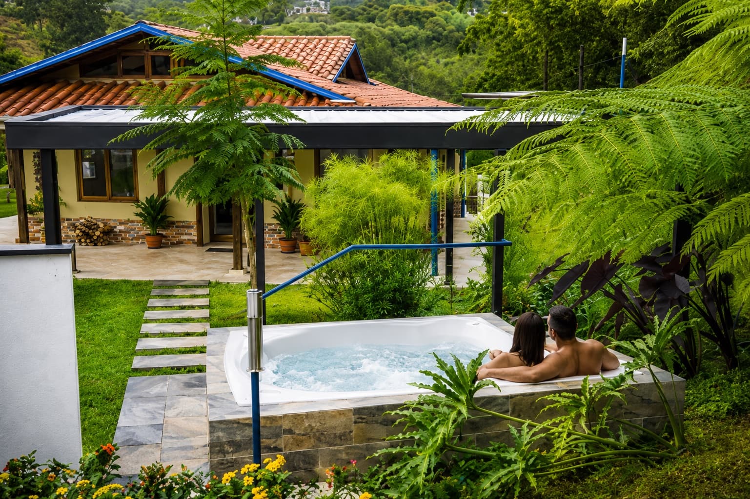 Pareja disfrutando el jacuzzi privado frente a la cabaña rodeada de jardines